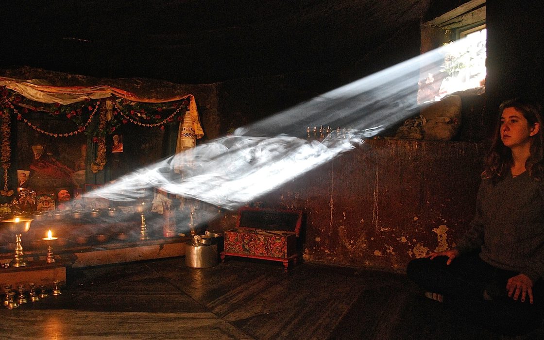 A student meditations in a dark room illuminated by a single shaft of light