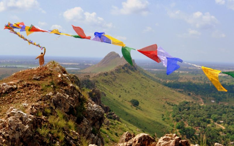 A man waves a string of bright cloth fabric in the wind on a mountain peak