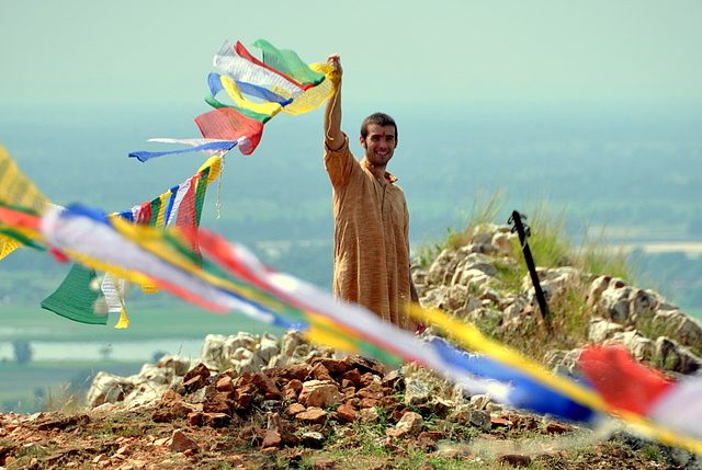 A man smiles while lifting a clothesline of bright cloth pieces