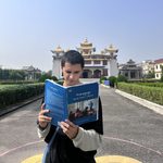 Student squints at a Tibetan language instruction book in front of a Buddhist temple