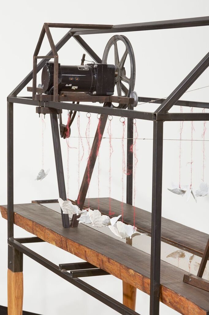 A motor mounted on a steel frame moves ceramic objects along a wooden table