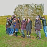 A group gathers in front of a rock at Avebury.