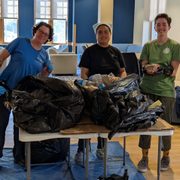 Five people stand behind a table where they will audit the contents of several black trash bags.