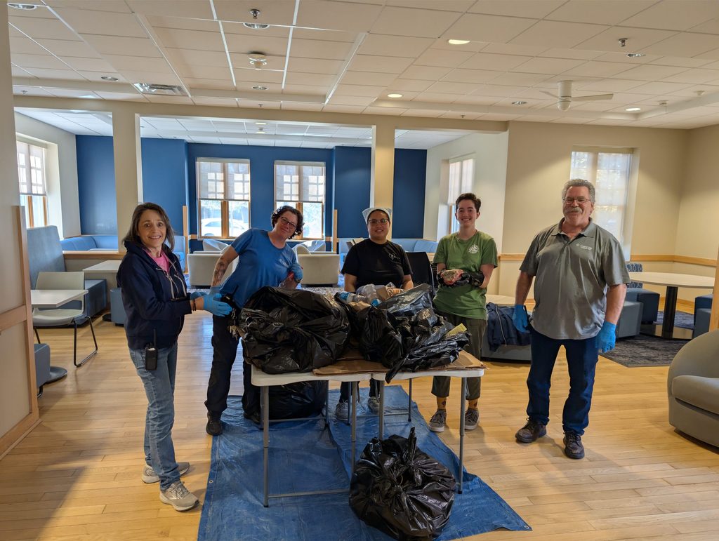 Five people stand behind a table where they will audit the contents of several black trash bags.