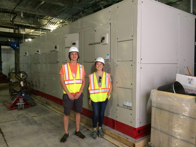 Two summer student interns standing in front of the new heat pump.