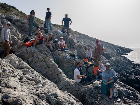 13 people sitting on a cliff near the ocean