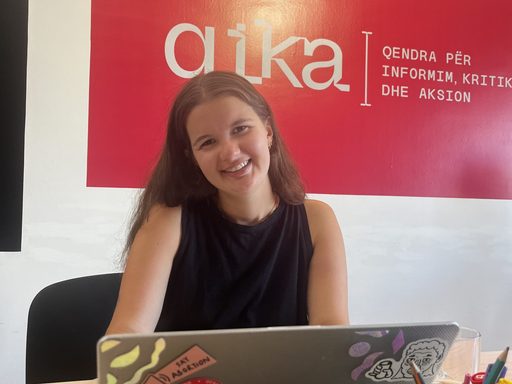 photo of woman sitting with a laptop in front of a red poster
