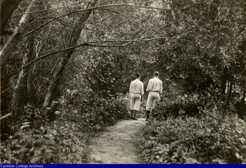 College students in dress typical of the 1920's walk a wooded path