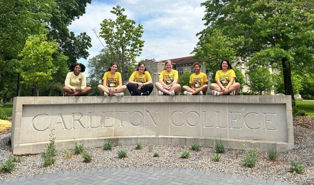 students seated on concrete carleton college entrance sign