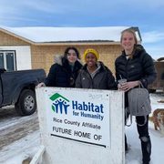 Three students standing behind Habitat for Humanity Sign