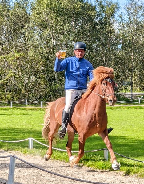 Person riding a horse while holding a mug of beer