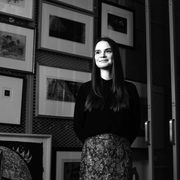 A woman with long hair stands in front of a wall of framed prints