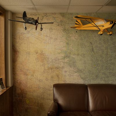 Two model airplanes, one black and one yellow, hang from the ceiling in an old building. A faded green and beige map covers the wall behind them