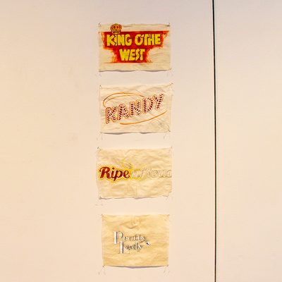 This work consists of sheets of paper tacked to the wall in columns. On the sheets are a series of phrases, some written only in pencil, others are filled in with red, yellow, and blue paint.