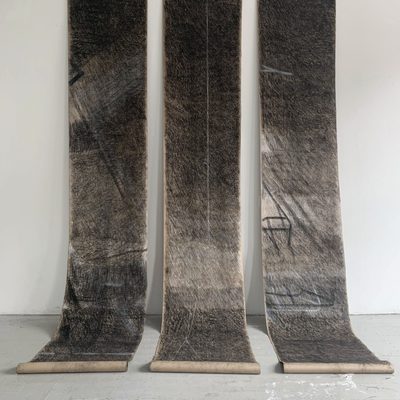 Three vertical scrolls hanging next to one another with black, gray, and white charcoal drawings with lines of varying degrees of thickness.