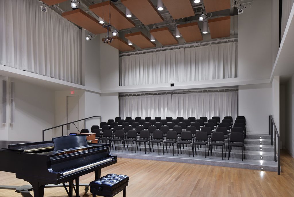 Photo of Applebaum Recital Hall, a choir rehearsal space, with piano, risers, and chairs.