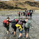 Carleton students walk across a stream together