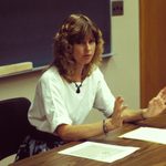 Bev nagel sitting at a desk in front of a classroom blackboard