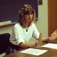 Bev nagel sitting at a desk in front of a classroom blackboard