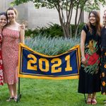 Four members of the Class of 2021 stand next to the maize and blue class banner, which reads 