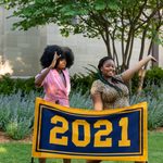 Two members of the Class of 2021 pose behind the maize and blue class banner, which reads 