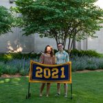 Two members of the Class of 2021 stand behind the maize and blue class banner, which reads 