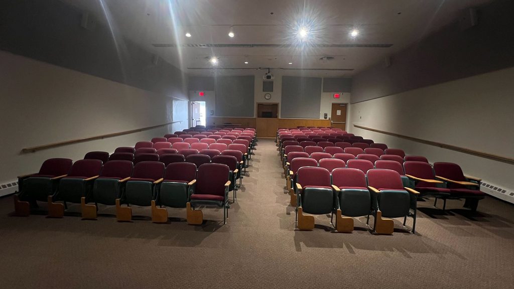 Boliou 104 auditorium, rear view showing rows of fixed seats and projection area.