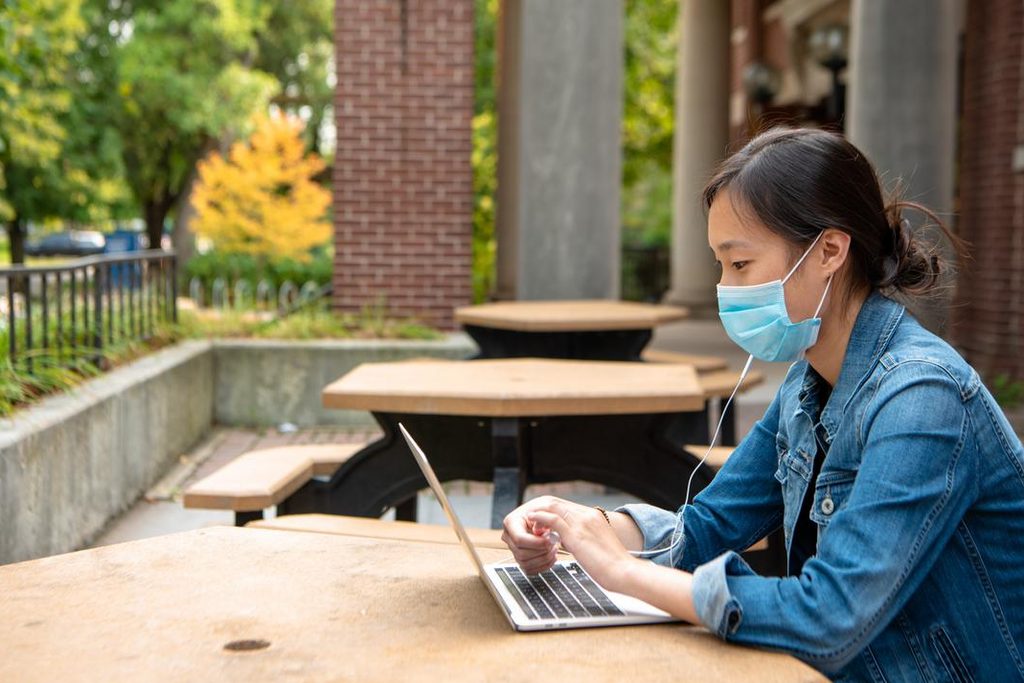 A student wearing a mask and using a laptop at an outdoor table