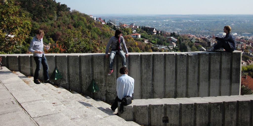 Four young men sit on a mountainside concrete wall