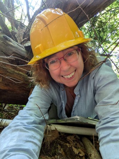 Photo of Audrey Barker-Plotkin wearing hard hat in a forest