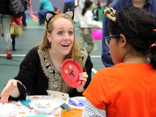 A student helps a child with crafts during Halloween Knights Carnival