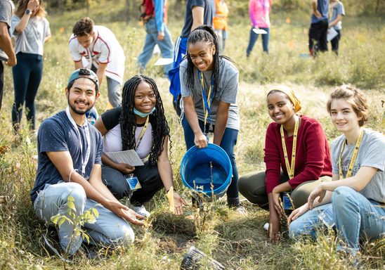 Smiling students planting trees in the arboretum