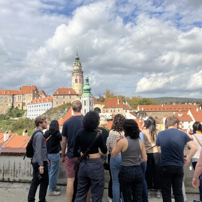 Students crowd around a low wall with a view of the town behind it, featuring church spires and Renaissance houses.