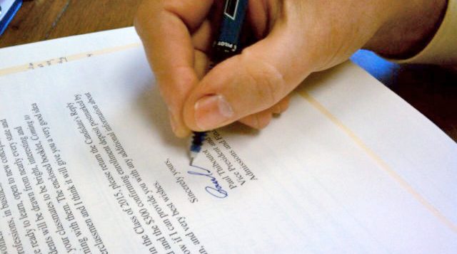 Close-up of a person signing their name on a document