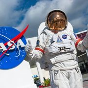 Astronaut giving a thumbs-up in front of NASA sign