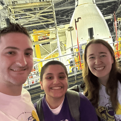 Three students standing in front of NASA rocket