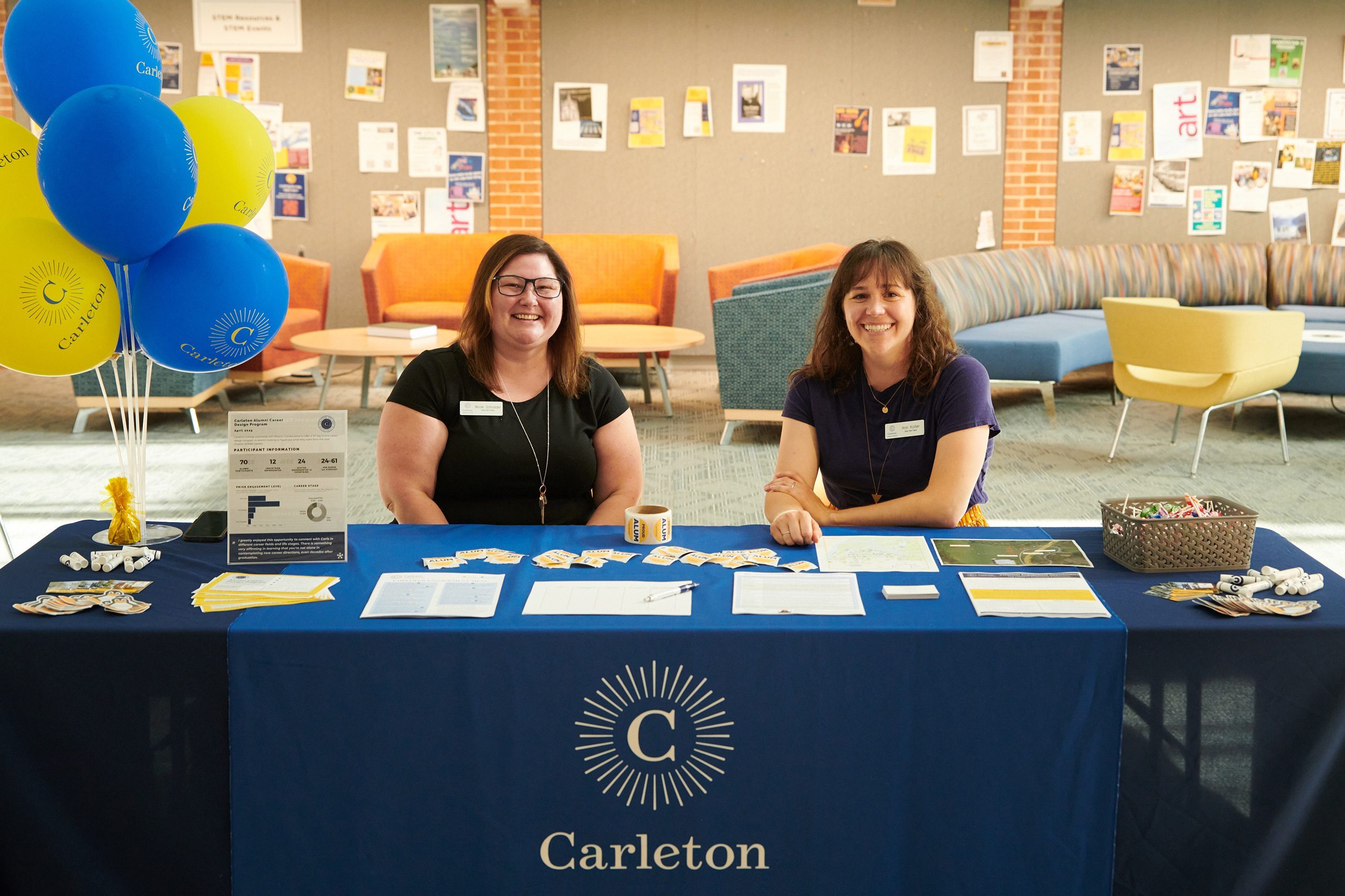 Two career center staff members at a registration table in Anderson Hall. There are balloons and stickers and candy and sign-up sheets on the table.