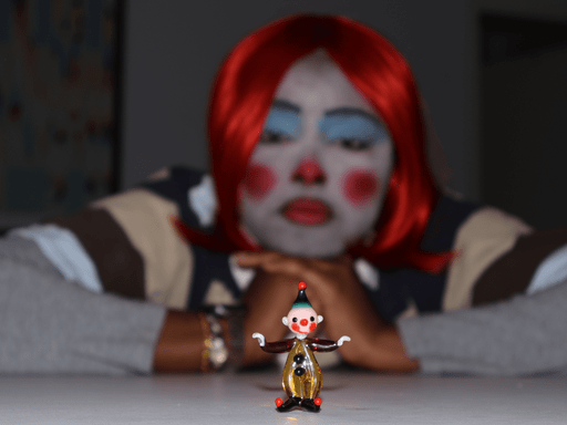 student in clown make up looks at figurine