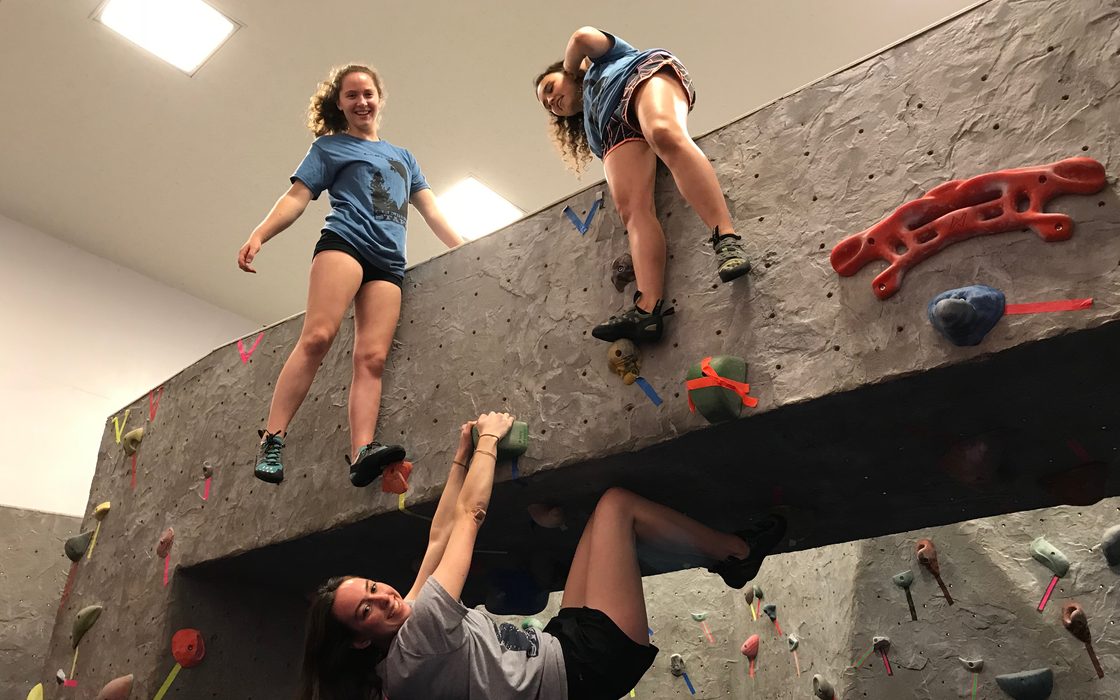 Three students climb a bouldering wall