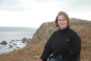 Professor Deborah Gross dressed in black outdoor apparel on the banks of several cliffs