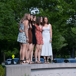 Five members of the Class of 2022 pose for a photo while standing on the Carleton College sign