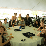 A large group poses for a photo at their table underneath the tent