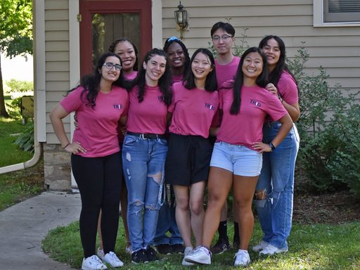 A group of students in matching pink t-shirts pose outside for a photo