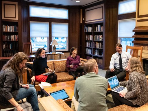 Faculty sit around a table in a book-filled room