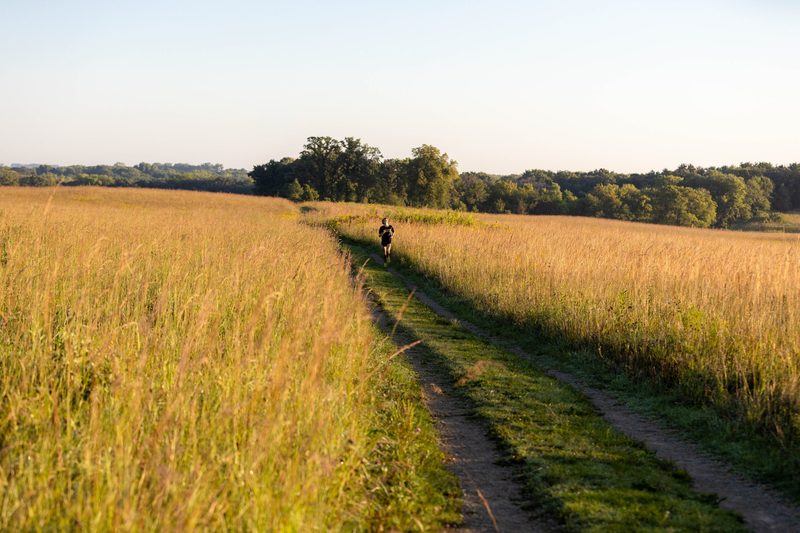 A person runs on a path that cuts through prairie land.
