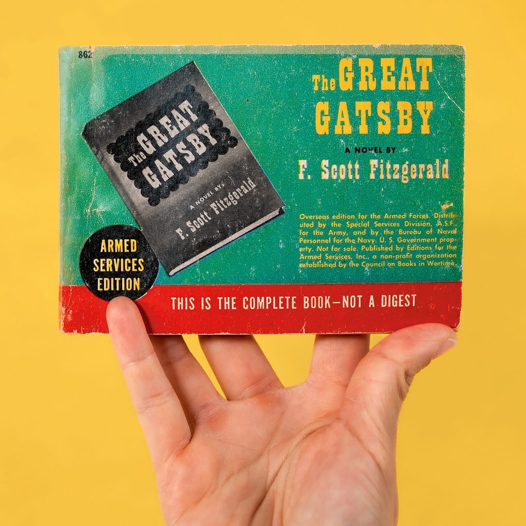 A hand holds a small copy of the Great Gatsby.