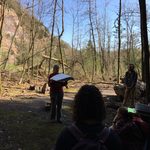 Students gathered in shadowy forest clearing learning from instructor