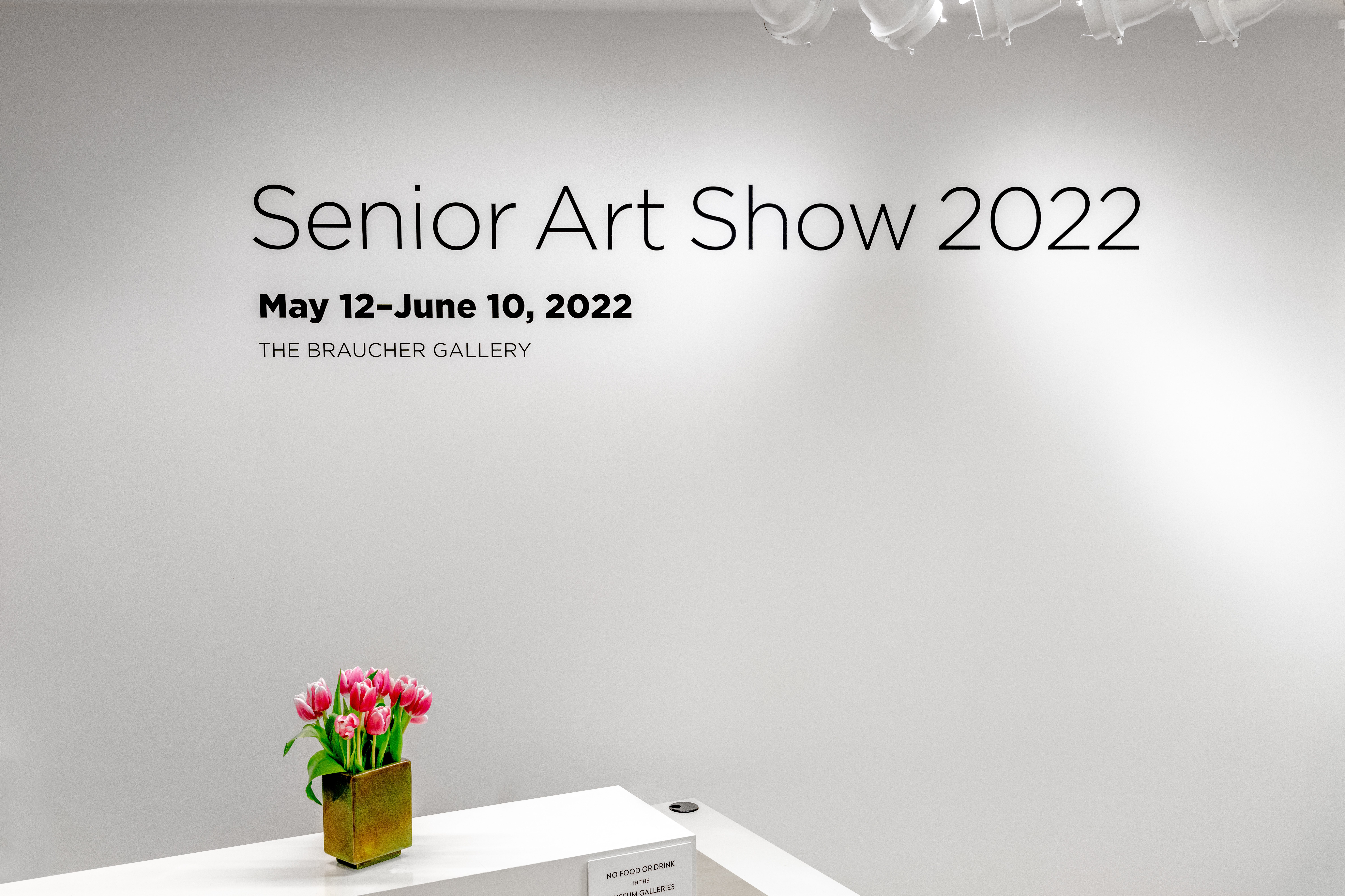 A photo of the front desk of the Perlman Teaching Museum with a bouquet of tulips and a sign saying “Senior Art Show 2022.”