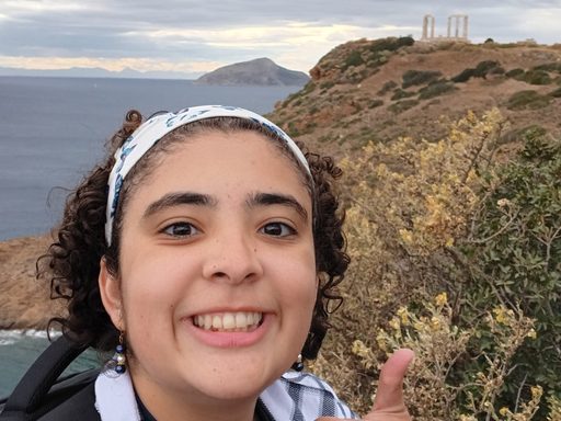 The author takes a selfie with the Temple of Poseidon from afar, as it was closed the day of the visit.