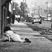 Film still showing a woman crawling along a grimy city sidewalk